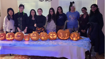Group of people posed behind a row of lit carved pumpkins on a table in a living room
